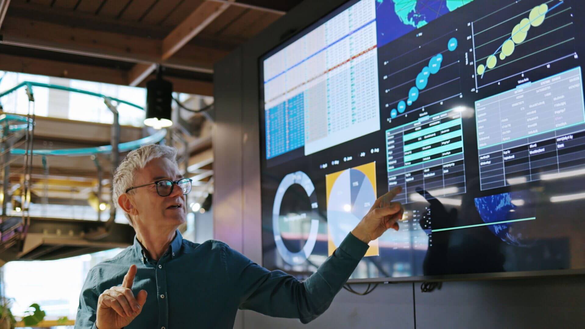 Man presenting data on large digital screen.